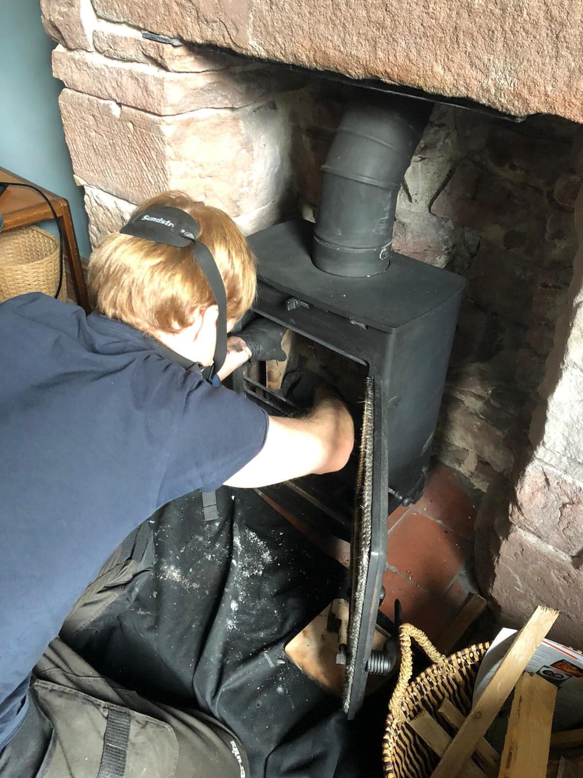 Brushing the flue of a stove set in a stone inglenook fireplace